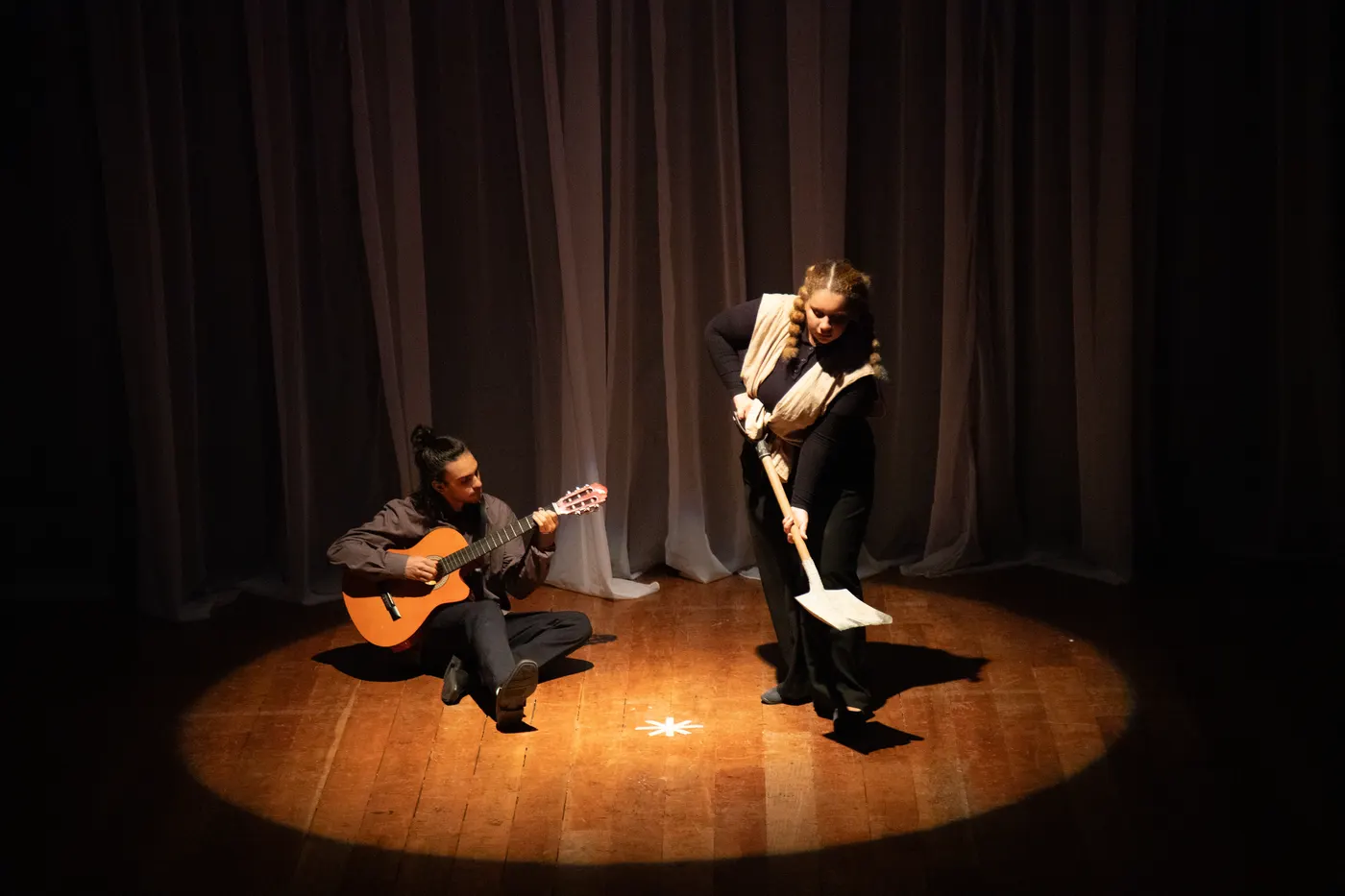 Dois atores em cena sob um foco de luz, um deles tocando violão